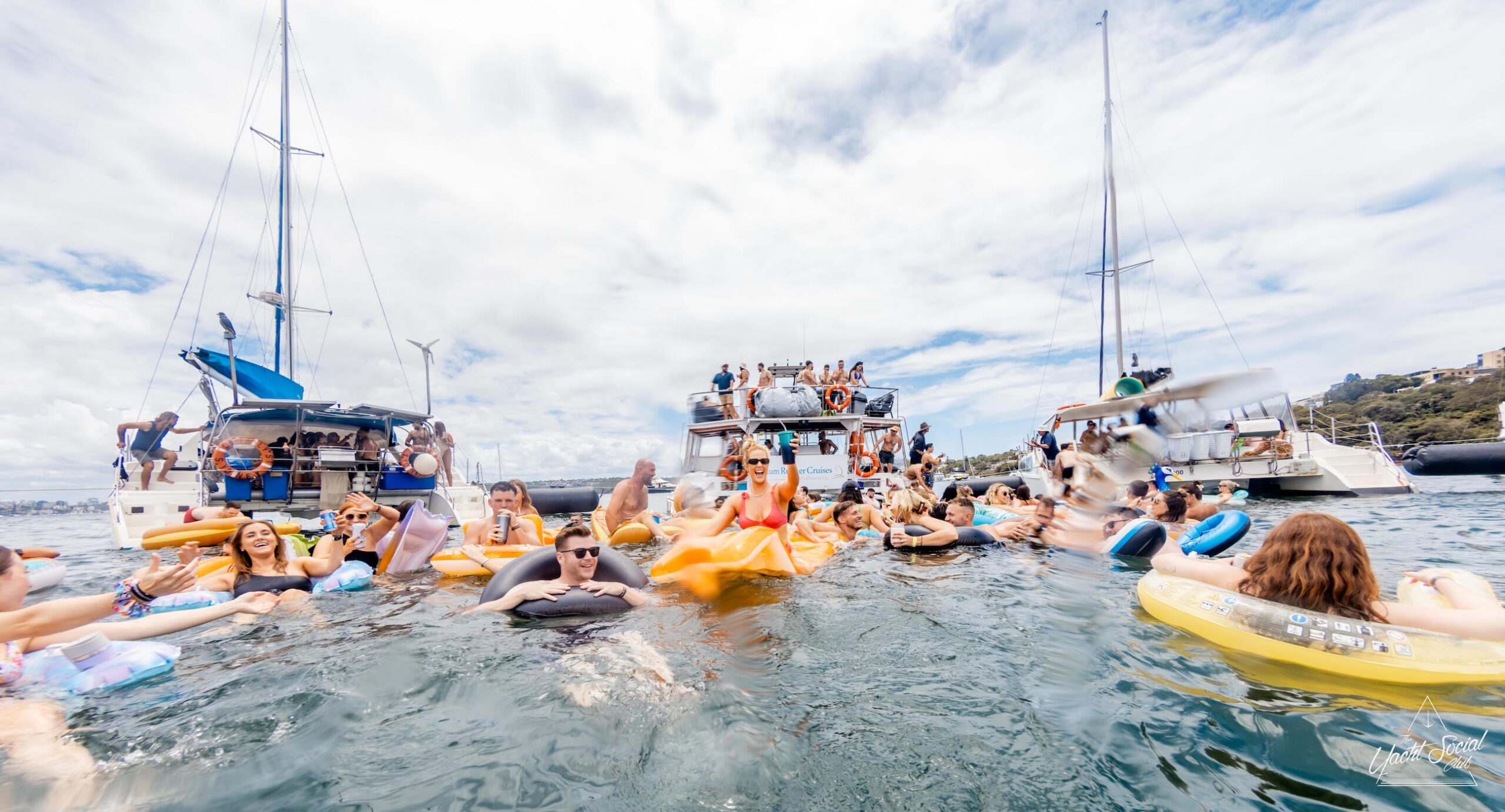People enjoy a sunny day on the water, swimming, and relaxing on inflatables near anchored boats during their private yacht charter in Sydney Harbour.