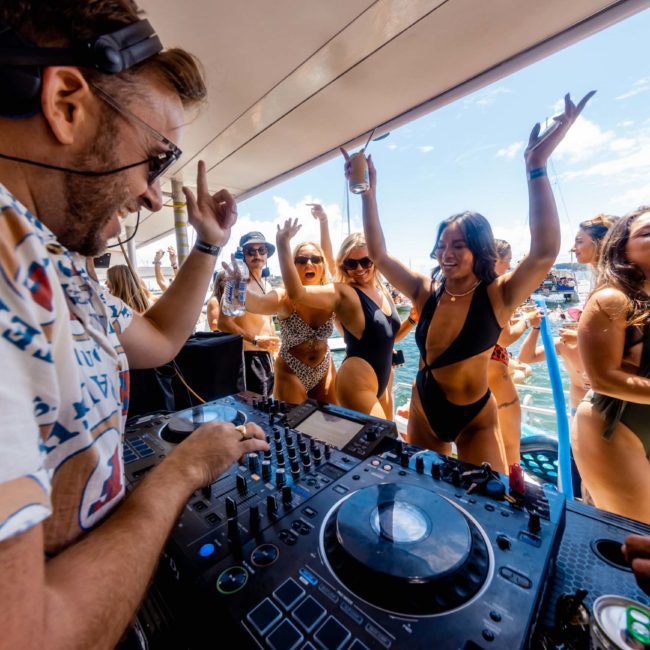A DJ is playing music on a luxury yacht hire Sydney while a group of people in swimwear dance and celebrate by the pool.