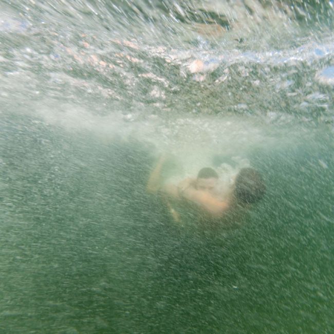 Underwater view of two people swimming, partially obscured by bubbles and water movement, enjoying a Sydney boat party hire experience.