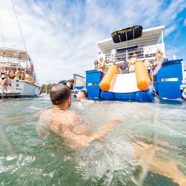 Enjoy a sunny day swimming near boats equipped with water slides, perfect for a Catamaran party Sydney experience or a private yacht charter in Sydney Harbour.