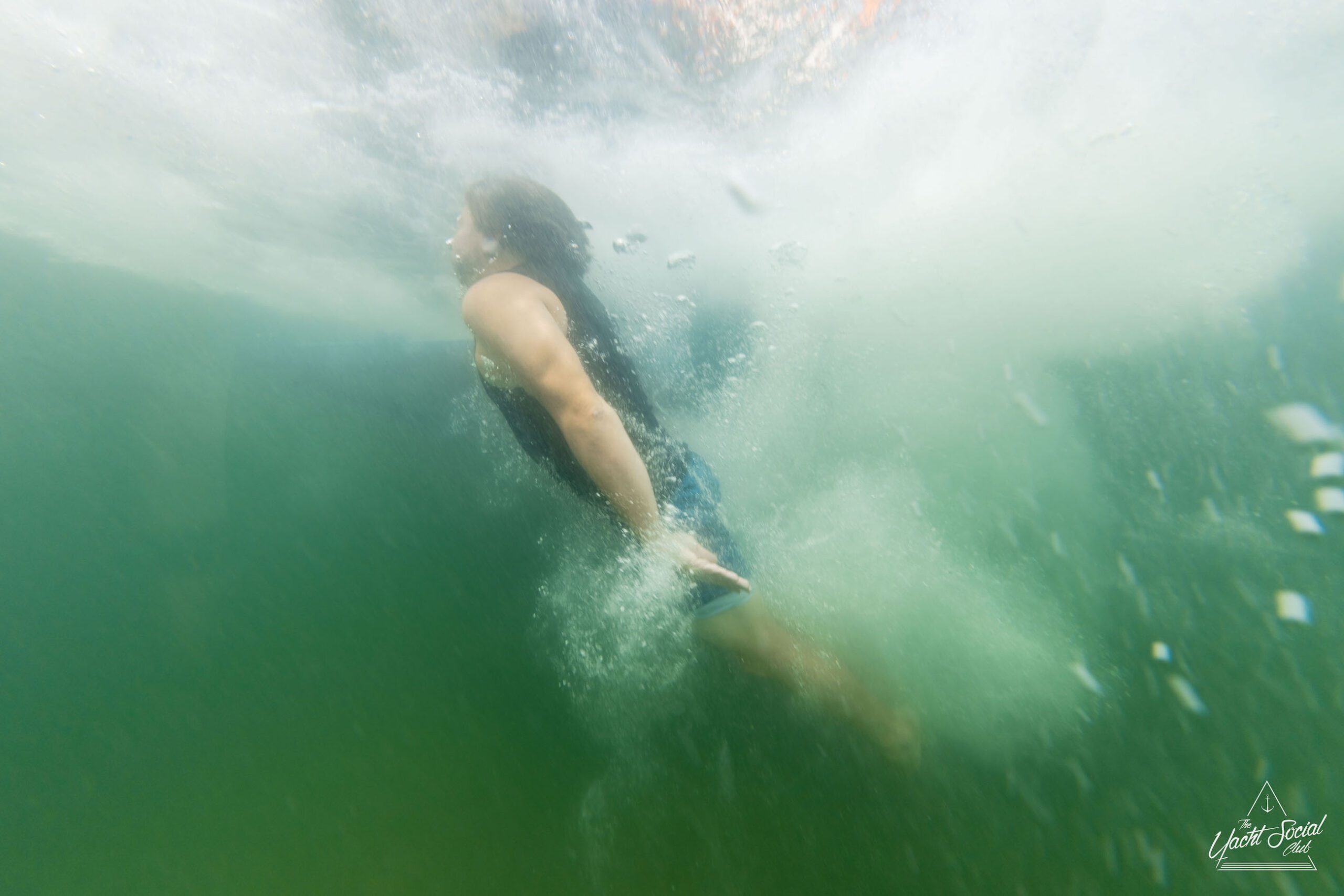 A person swimming underwater with arms by their side in greenish water, creating bubbles and splashes. Perfect for cooling off after a private yacht charter Sydney Harbour.