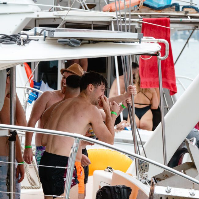 A group of people enjoying a day on a boat. Several individuals are in swimwear, some standing while others sit leisurely. Towels and other boating equipment are visible. The weather is warm and sunny, creating a lively and festive atmosphere perfect for paddleboarding.