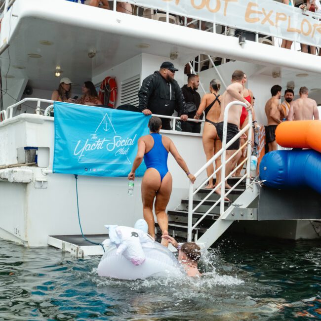 A group of people on a yacht participate in a lively social event. Some are on the deck, while others climb the stairs from the water. A person in a blue swimsuit enjoys an inflatable unicorn raft in the water. A banner reads "Yacht Social Extravaganza.