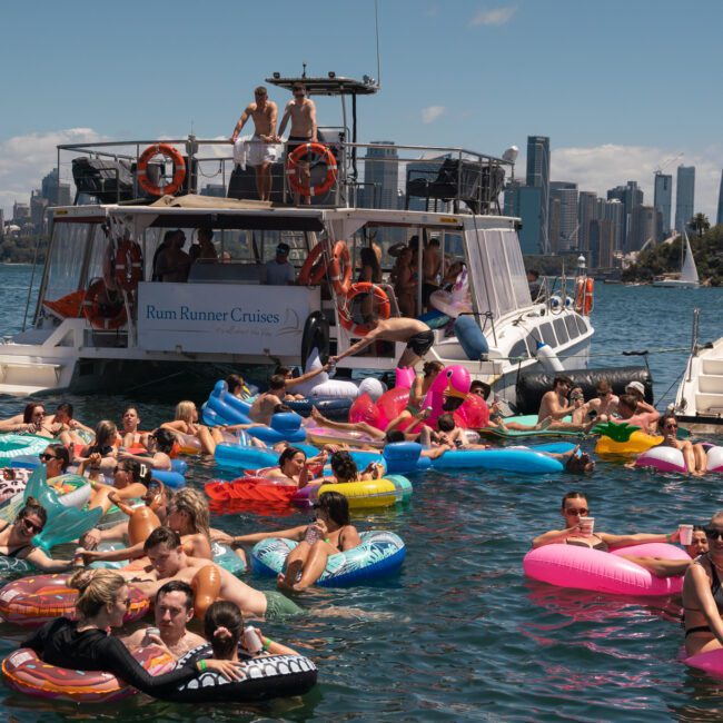 People on colorful inflatables and boats enjoying a sunny day on the water with a city skyline in the background, enhanced by a lively catamaran party Sydney.