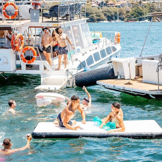 People enjoying a sunny day on a luxury yacht hire Sydney, with some swimming and playing in the water while others relax on boats.