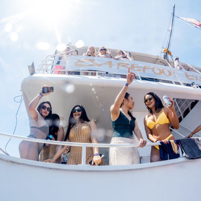 People are standing and taking photos on the upper decks of a boat under a bright sunlit sky, enjoying what looks like an amazing Sydney boat party hire.
