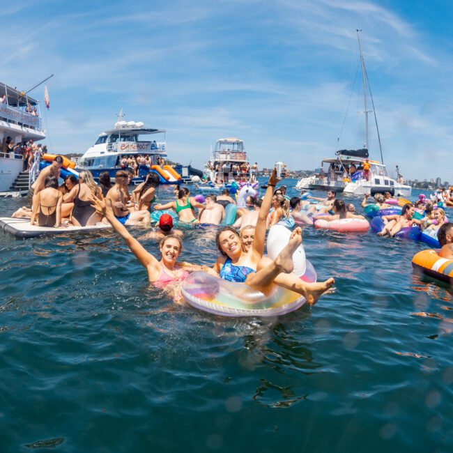 People are enjoying a sunny day, floating in the water on inflatables, surrounded by multiple yachts from a private yacht charter Sydney Harbour.