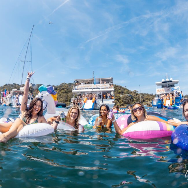 A group of people on inflatable floats enjoying a day on the water with boats and other people in the background, perfect for a Catamaran party Sydney or kicking it up with DJ boat hire Sydney.