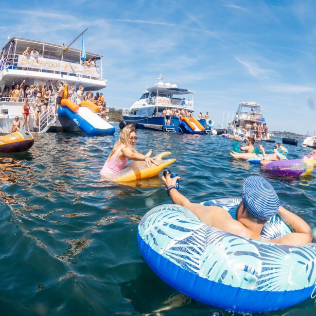 People floating on inflatable tubes in the water near anchored boats, enjoying a sunny day at a Catamaran party in Sydney.