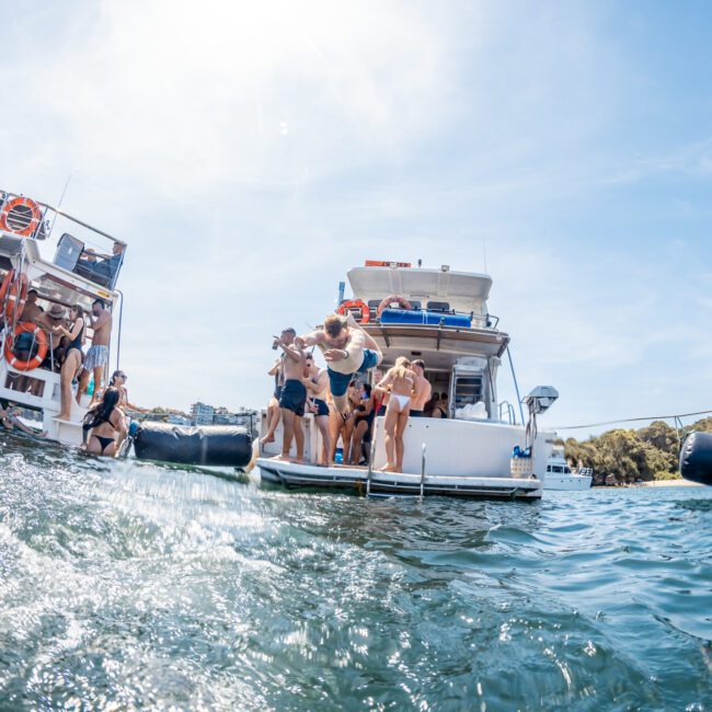People enjoying time on two docked boats in the water on a sunny day, taking advantage of Luxury yacht hire Sydney for an unforgettable experience.