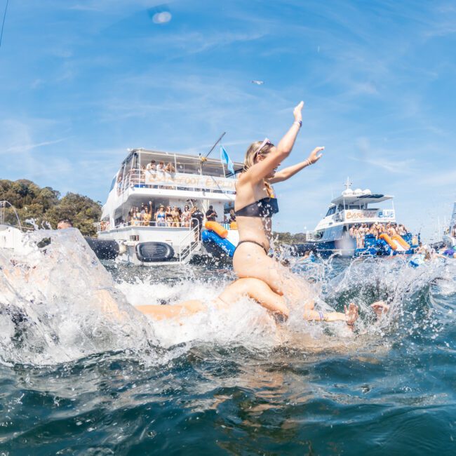 People enjoying a sunny day on the water, splashing and having fun near moored boats, with a Yacht Social Club logo in the bottom right corner. Perfect for those interested in private yacht charter Sydney Harbour or hosting luxury yacht hire Sydney events.