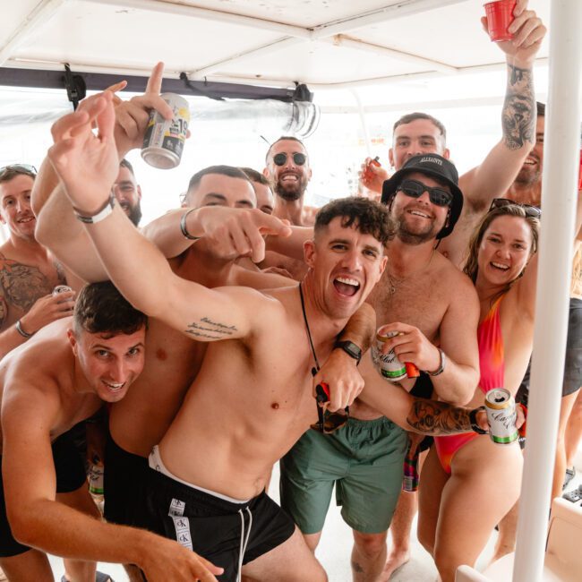 A group of people in swimwear, appearing to have fun on a boat. They are smiling, raising drinks, and posing for the camera. The atmosphere is lively and celebratory, suggesting they are enjoying a party with Luxury Yacht Rentals Sydney or Boat Parties Sydney The Yacht Social Club on the water.