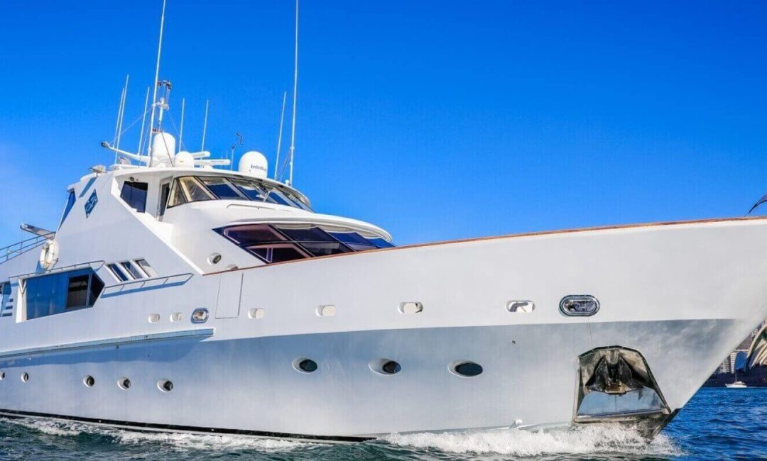 A large luxury yacht cruises on a sunny day with a clear blue sky. The yacht is white with multiple decks and various antennas. The Sydney Opera House is visible in the background, indicating the yacht is in Sydney Harbour for a lively Boat Rental and Parties Sydney The Yacht Social Club event.
