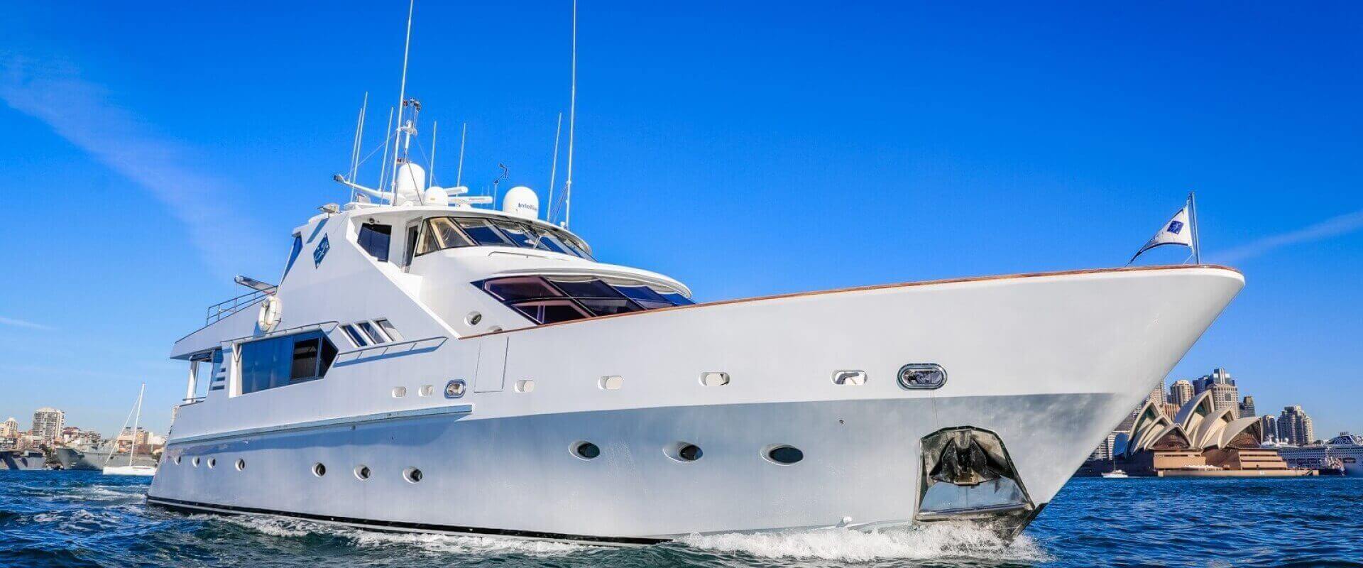A large luxury yacht cruises on a sunny day with a clear blue sky. The yacht is white with multiple decks and various antennas. The Sydney Opera House is visible in the background, indicating the yacht is in Sydney Harbour for a lively Boat Rental and Parties Sydney The Yacht Social Club event.