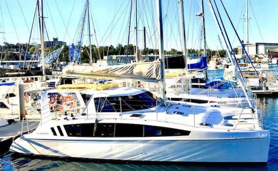 A marina filled with several docked sailboats. Prominently in the foreground is a large white sailing yacht with a modern design, its sails furled. The background reveals a variety of other boats and waterfront facilities. It is a bright, sunny day—perfect for enjoying Luxury Yacht Rentals Sydney.