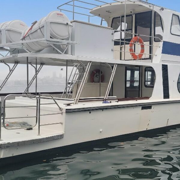 Caitlin’s Yacht, a white boat with blue details, floats on calm water near a hazy city skyline. Two decks, life rings, and rafts are visible—an ideal scene for using your Caitlin's Yacht Ticket.