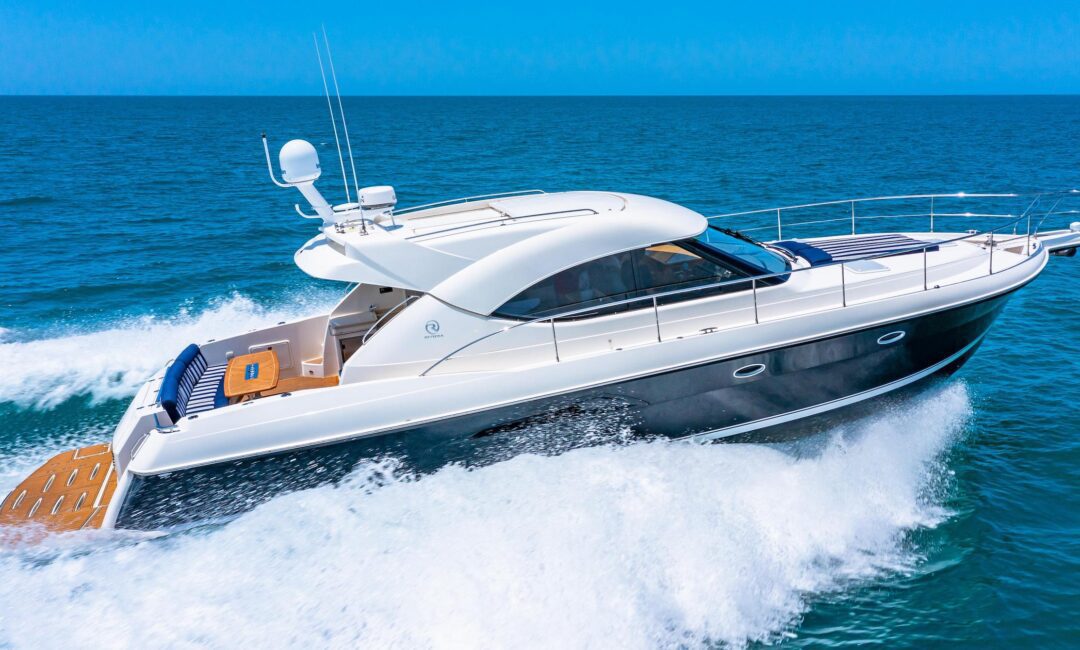 A sleek white and black motor yacht speeds across a calm blue ocean, creating foamy waves behind it under a clear sky.