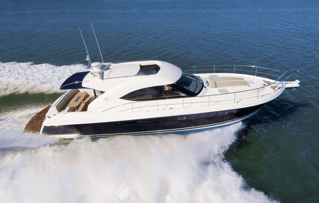 A sleek, modern motor yacht with a white top and dark hull speeds across blue water, creating a large wake behind it on a sunny day.