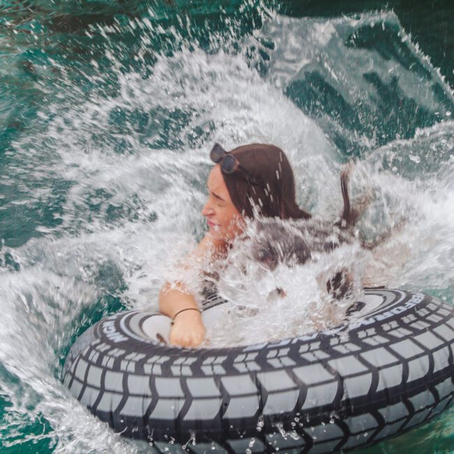 A person splashes into green water while holding onto a black and white tire-shaped float. Water sprays around them as they enjoy the moment.