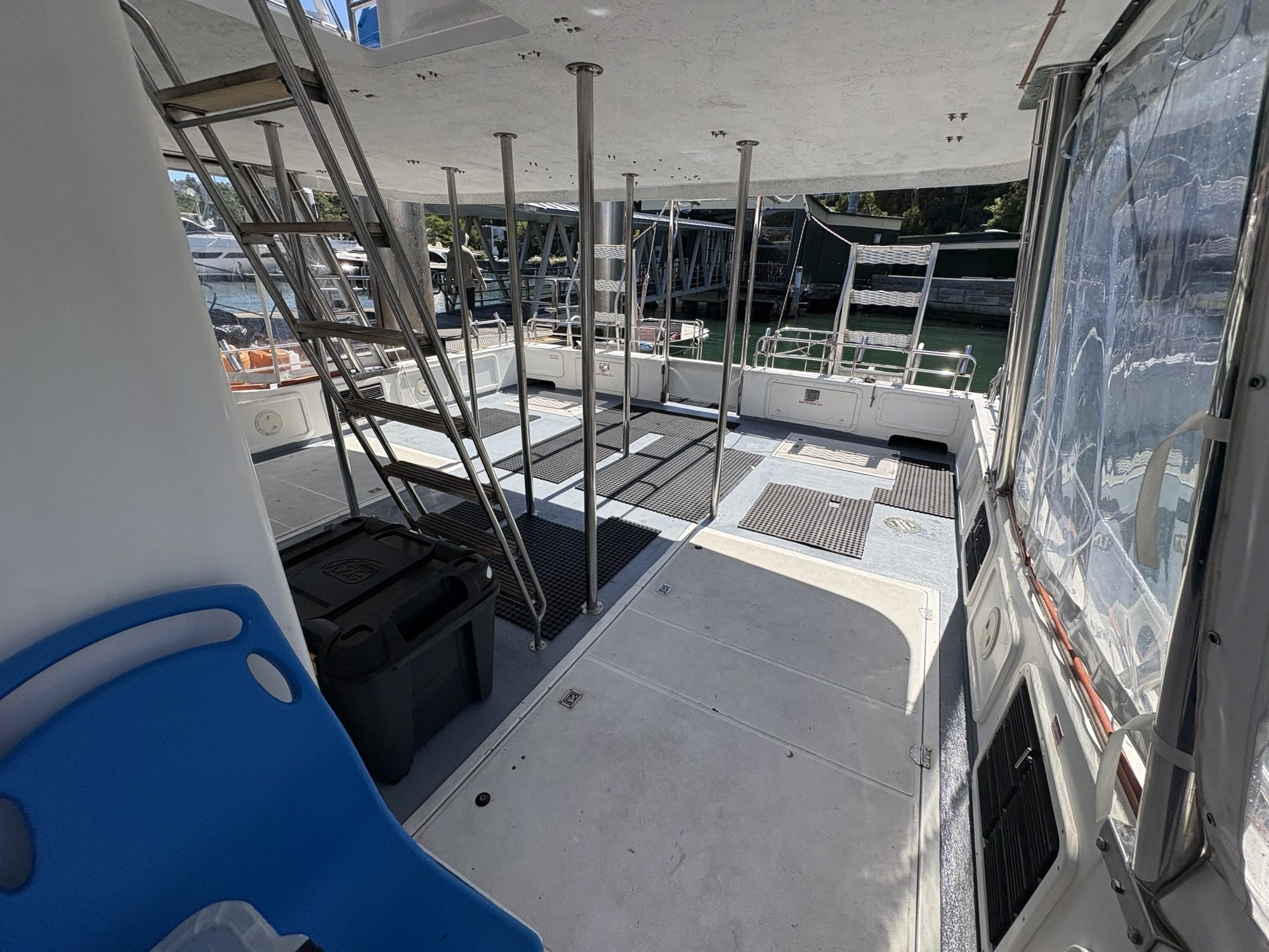Arcadia’s open deck features metal poles, black floor mats, a blue seat on the left, and plastic bins. Water and docks are visible through clear plastic coverings in the background.
