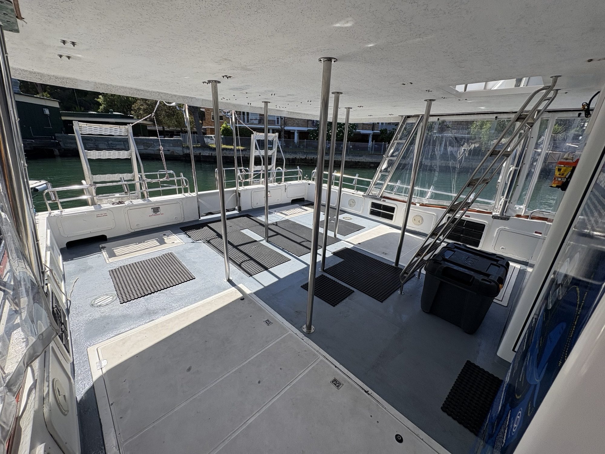 The Arcadia features a spacious covered deck with metal poles, black floor mats, side benches, and water views beyond the railing. Sunlight brightens the area through clear side panels.