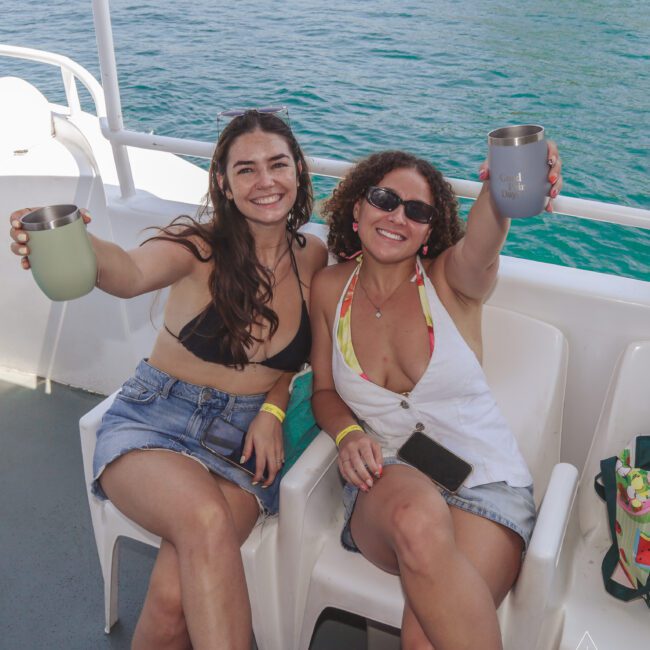 Two women sitting on a boat holding cups.